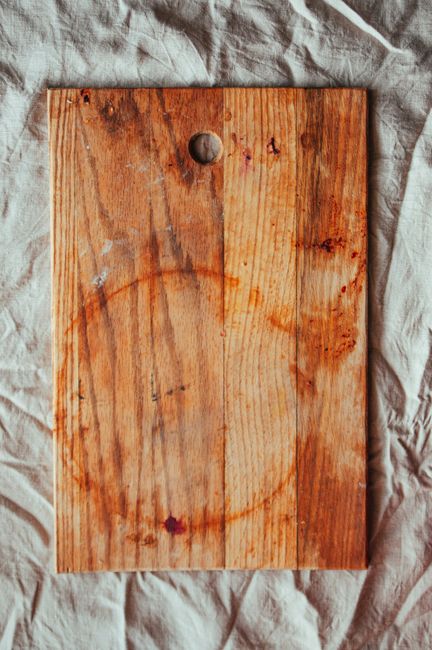 A close-up view of a hardwood floor being cleaned with a green mop attached to a handle. The mop head features a textured, absorbent cleaning pad that appears to be slightly worn. The floor surface is